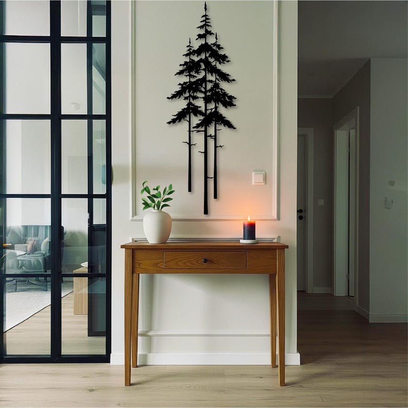 May include: A wooden console table with a drawer and a white vase with greenery on top. A black metal tree silhouette hangs on the wall above the table. A lit candle sits on the table, adding a warm glow to the room.