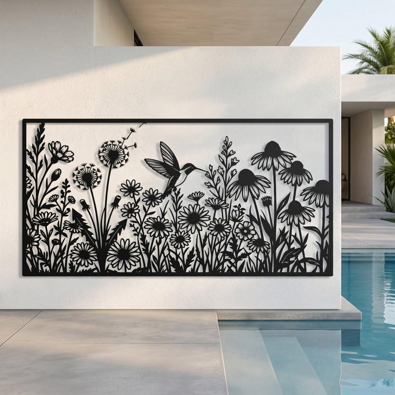 May include: A rectangular black metal wall art piece featuring a laser-cut design of a hummingbird hovering among various wildflowers, including dandelions and daisies, enclosed within a thin, solid black frame border.