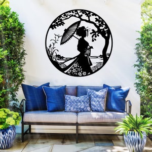 May include: Black metal wall art featuring a silhouette of a woman in a kimono holding an umbrella, standing in front of a tree and a body of water. The art is circular and has a decorative design.