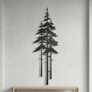 May include: Black metal wall art depicting a cluster of stylized pine trees. The artwork features a minimalist design with detailed branches and needles, creating a natural, forest-inspired aesthetic. The piece is mounted on a textured white wall.