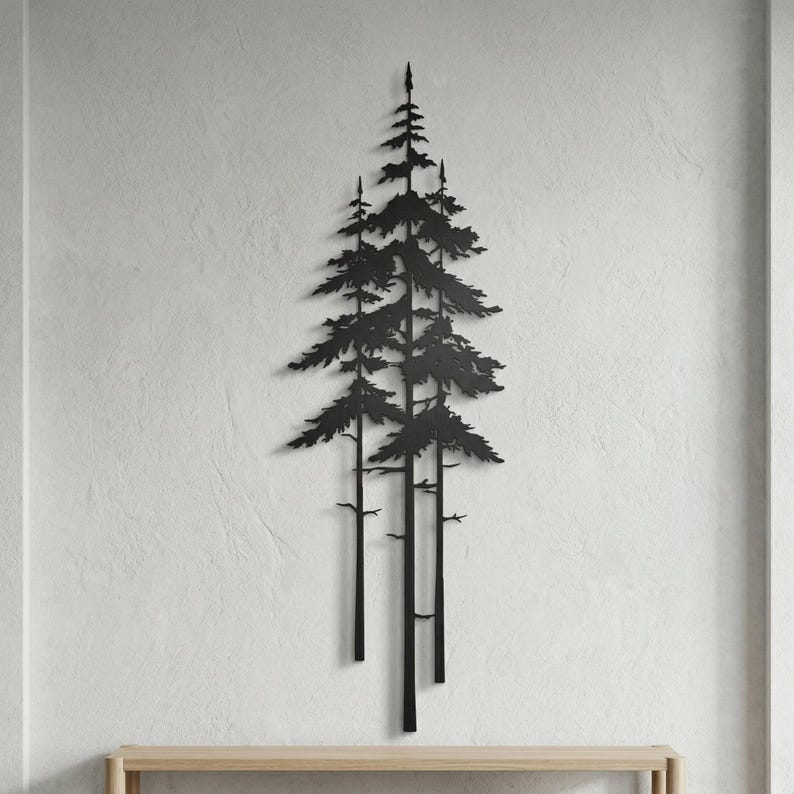 May include: Black metal wall art depicting a cluster of stylized pine trees. The artwork features a minimalist design with detailed branches and needles, creating a natural, forest-inspired aesthetic. The piece is mounted on a textured white wall.