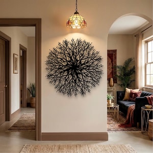 May include: A black metal tree-like wall art decorates a beige wall. A stained glass pendant light hangs above the art. The room has a neutral color palette with a rug and a sofa in the background.