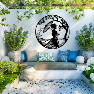 May include: A black metal wall decor featuring a silhouette of a woman holding an umbrella, standing in a garden setting. The decor is hanging on a white wall in a patio setting with lush greenery and potted plants.