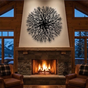 May include: A black metal tree branch wall art decor is mounted above a stone fireplace with a burning fire. The art piece is circular and has a detailed branch design. Two leather armchairs are in front of the fireplace.