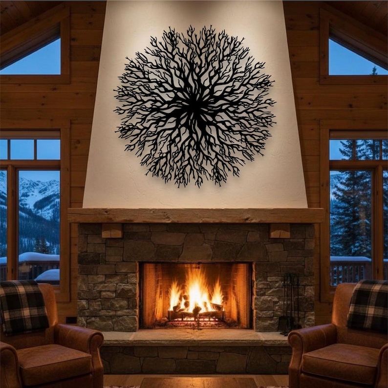 May include: A black metal tree branch wall art decor is mounted above a stone fireplace with a burning fire. The art piece is circular and has a detailed branch design. Two leather armchairs are in front of the fireplace.