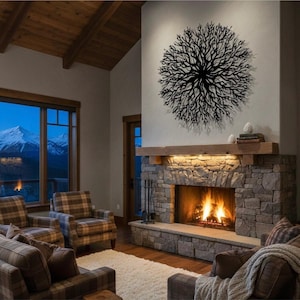 May include: A cozy living room with a stone fireplace and a burning fire. Above the fireplace is a wooden mantel and a large, circular, black metal wall art piece. The room has plaid furniture and a view of mountains through the window.