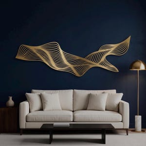 Puede incluir: Una gran pieza de arte mural horizontal de metal dorado que presenta una serie de líneas onduladas paralelas y fluidas. La escultura está montada en una pared azul marino oscuro sobre un sofá de color crema con cuatro cojines a juego.