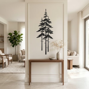 May include: Black metal wall art depicting a cluster of stylized pine trees. The artwork is mounted on a white wall above a wooden console table. The room features neutral tones and natural light, with a modern aesthetic.