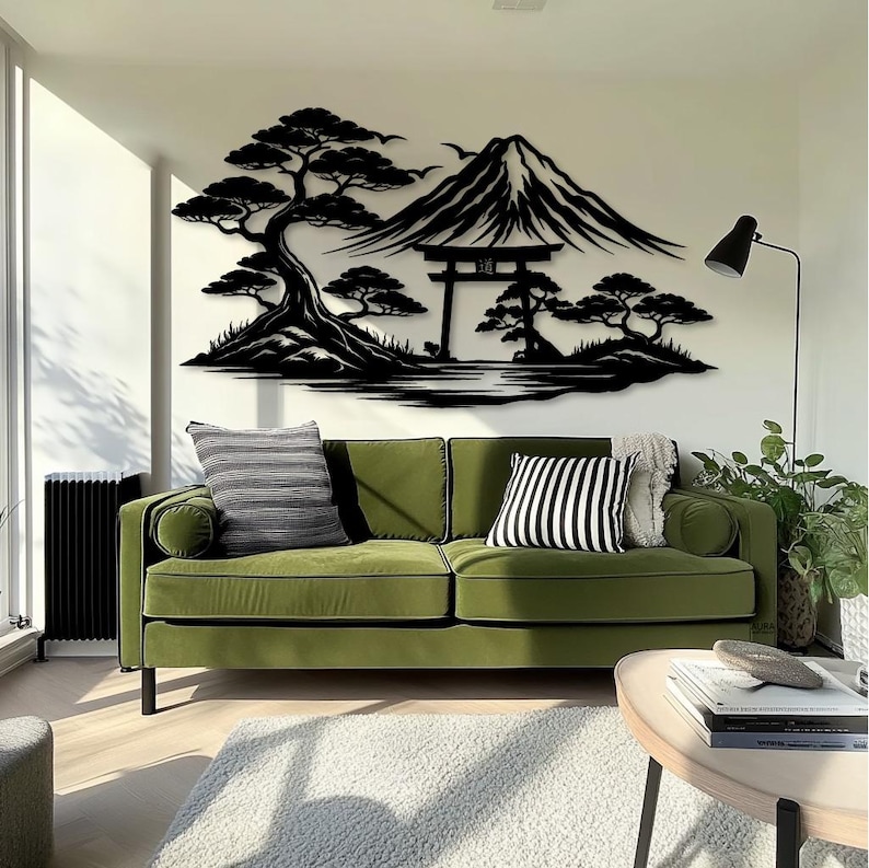 May include: A black metal wall art piece depicting a Japanese landscape with a mountain, trees, and a traditional gate. The art is mounted on a white wall above a green sofa with decorative pillows. A black floor lamp and a round wooden table are also visible.
