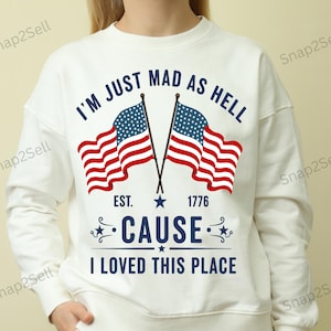 May include: White sweatshirt with the text "I'M JUST MAD AS HELL CAUSE I LOVED THIS PLACE" and two American flags. The sweatshirt also has the text "EST. 1776". The design is in red and blue.