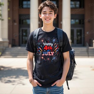 May include: A black short-sleeved t-shirt featuring a graphic print of colorful fireworks and the text Happy 4th of JULY with the word JULY styled in a red, white, and blue American flag pattern, worn with a dark backpack and blue denim jeans.