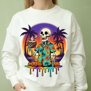 Könnte beinhalten: Weißes Sweatshirt mit einem Skelett in einem Hawaiihemd, das ein Kokosnussgetränk hält. Das Design umfasst Palmen, Kürbisse und einen Sonnenuntergang. Der untere Teil des Designs hat tropfende Farbe.