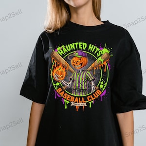 Puede incluir: Camiseta negra con un diseño de Halloween. El diseño presenta un esqueleto con cabeza de calabaza con uniforme de béisbol y sosteniendo un bate y una pequeña calabaza. El texto dice "Haunted Hits Baseball Club, Founded 2026."