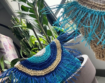 May include: A blue, white, and beige crocheted bag with fringe. The bag is in the shape of a half-circle and has a woven design.