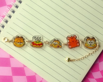 May include: A gold chain bracelet with clear plastic charms featuring cartoon images of Garfield, lasagna, and a teddy bear.