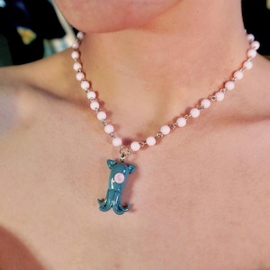 Peut inclure: Un collier avec un pendentif calmar turquoise orn&eacute; d'un cercle rose, suspendu &agrave; une cha&icirc;ne de petites perles rose clair. Un bijou unique.
