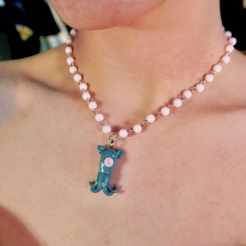 Peut inclure: Un collier avec un pendentif calmar turquoise orn&eacute; d'un cercle rose, suspendu &agrave; une cha&icirc;ne de petites perles rose clair. Un bijou unique.