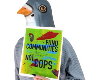 May include: A person wearing a gray pigeon mask holding a sign with the words "FUND COMMUNITIES NOT COPS" in blue and white text on a green background with red and black abstract shapes.