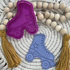 May include: Two roller skate cookie cutters, one purple and one blue. The purple roller skate has a star on the side. The blue roller skate has a star on the toe.