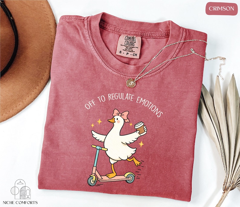 A red t-shirt with a cartoon image of a duck riding a scooter, accompanied by the text "Off to regulate emotions".