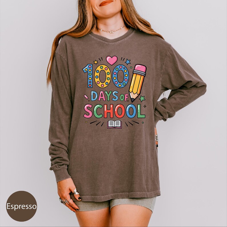 A woman wearing a long-sleeved shirt with a colorful graphic design that says "100 DAYS OF SCHOOL" printed on it.
