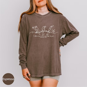 A woman wearing a long-sleeved shirt with a graphic design of three birds and text below it.