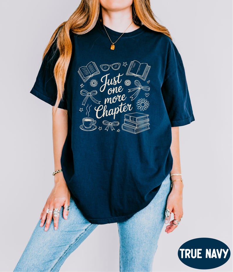 A woman wearing a navy blue t-shirt with the text "Just one more chapter" printed on it, along with various icons and symbols related to reading and writing.