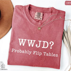 a red t-shirt with the text "WWJD? probably Flip Tables" printed on it, along with a necklace and a hat.