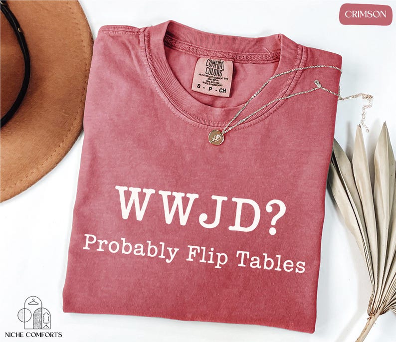 a red t-shirt with the text "WWJD? probably Flip Tables" printed on it, along with a necklace and a hat.