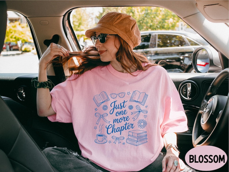 A woman wearing a pink t-shirt with a graphic design and text, sitting in the passenger seat of a car.