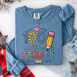 A blue long-sleeved t-shirt with a graphic design celebrating the 100th day of school, along with a pair of jeans and star-shaped embellishments.