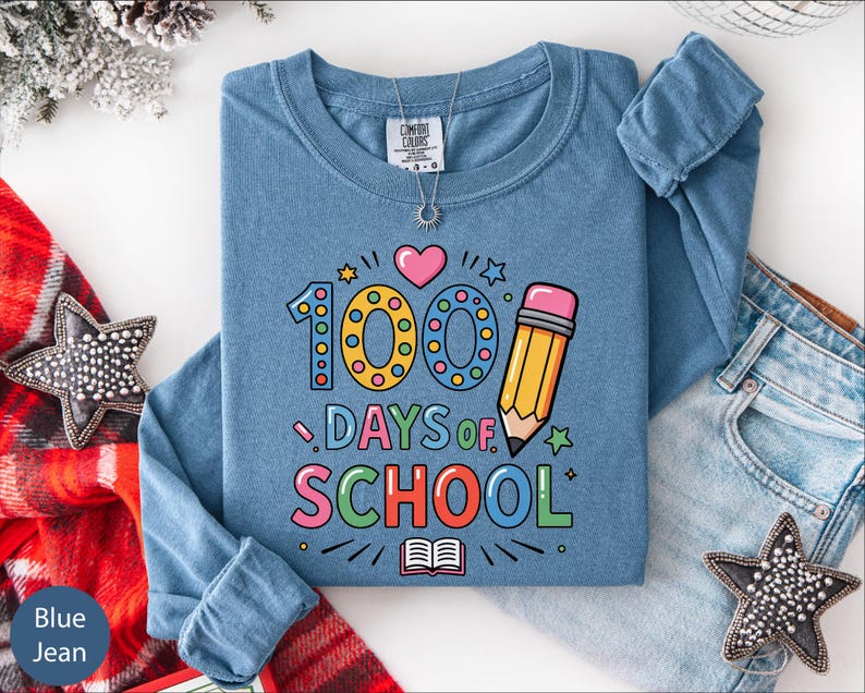 A blue long-sleeved t-shirt with a graphic design celebrating the 100th day of school, along with a pair of jeans and star-shaped embellishments.