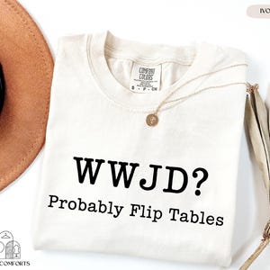 a white t-shirt with the text "WWJD? probably Flip Tables" printed on it, along with a necklace and a hat.