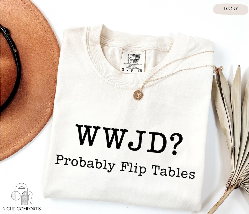a white t-shirt with the text "WWJD? probably Flip Tables" printed on it, along with a necklace and a hat.