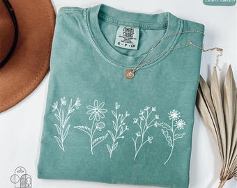 May include: A light green t-shirt with a white outline of five different flowers. The shirt has a tag that says "Comfort Colors" and "S - P - Ch".