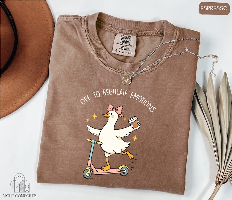 a brown t-shirt with a cartoon image of a duck riding a scooter, accompanied by the text "Off to regulate emotions".