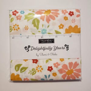May include: A fabric bundle featuring a floral pattern with pink, orange, blue, and green flowers on a white background. The package is labeled "Delightfully Yours" by Sherri & Chelsi, with a ruler printed on the packaging.