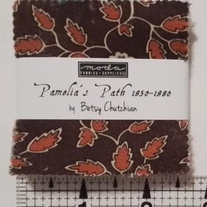 May include: A stack of fabric squares with a dark brown background and a repeating pattern of orange leaves and vines. The fabric is labeled "Pamelia's Path 1850-1880 by Betsy Chutchian". A ruler shows the fabric is approximately 2 inches wide.