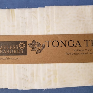May include: A package of 42 white cotton fabric squares, each 5" x 5", with a subtle pattern. The label reads "TONGA TREAT" and "Timeless Treasures". The fabric is 100% cotton and made in Indonesia.