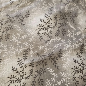 May include: Close-up of fabric with a repeating pattern of stylized vines and leaves. The design features dark brown and white foliage against a mottled gray background, creating a textured appearance. The fabric has a soft, muted color palette.