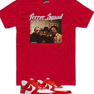 Puede incluir: Camiseta roja con la frase "Terror Squad" y un gráfico de tres personajes de películas de terror. La imagen también incluye un par de zapatillas rojas y blancas.