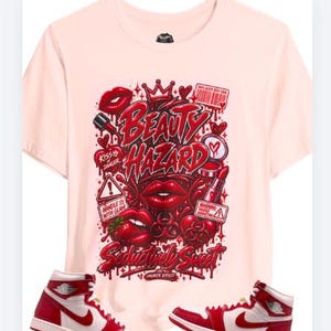 Può includere: Una t-shirt rosa chiaro con una stampa grafica che riporta il testo "BEAUTY HAZARD" e "SEDUCTIVELY SWEET" in rosso, circondato da illustrazioni di labbra, una corona, rossetto e segnali di pericolo, abbinata a due sneakers alte rosse e bianche.