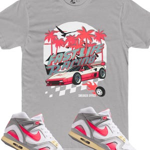 Op de afbeelding: Een paar witte en grijze Nike sneakers met roze accenten. De sneakers liggen op een grijs t-shirt met een afbeelding van een rode sportwagen en palmbomen. De afbeelding zegt "Fast Life Racing" en "Sneaker Effect".