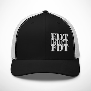 Puede incluir: Gorra de camionero negra y blanca con las letras "FDT" bordadas en blanco, apiladas tres veces. La gorra tiene una visera y una parte delantera negras, y una parte trasera de malla blanca para la ventilación.