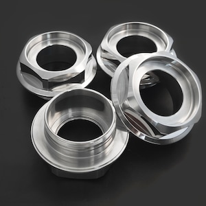 Puede incluir: Cuatro tapas de metal plateado con bordes hexagonales y un interior liso y redondeado. Las tapas están apiladas sobre una superficie negra.