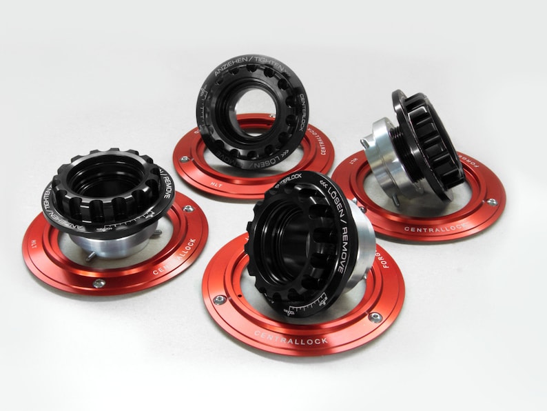 May include: Four black and silver central locking wheel nuts with red aluminum rings. The rings have the words "Centrallock" and "Losen/Remove" printed on them.