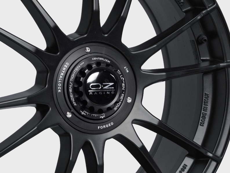 May include: Black forged aluminum car wheel with a silver OZ Racing logo and the text "CENTRALLOCK ANZIEHEN/TIGHTEN >>>>>>> CENTERLOCK" and "MADE IN ITALY".