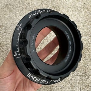 May include: Black metal wheel hub with a torque wrench, a white gauge marked in Nm, and the text "ANZIEHEN", "NO 22/10/2024", "MG LINE BBS CENTERLOCK.COM", "SPEN / REMOVE", and "STOP".
