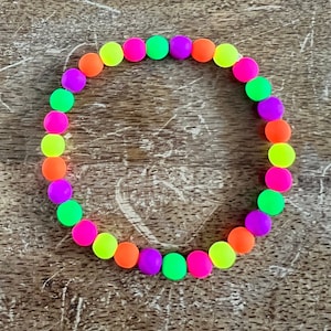 May include: A neon colored beaded bracelet with alternating colors of green, purple, orange, yellow, and pink.