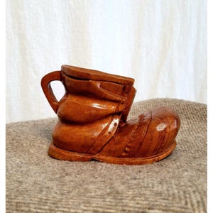 May include: A wooden boot-shaped trinket box with a hinged lid and a handle. The box is carved in a rustic style and has a dark brown finish.